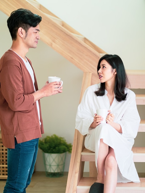 Une jeune femme et un homme asiatiques aiment passer du temps ensemble à la maison avec une tasse de café dans les mains.