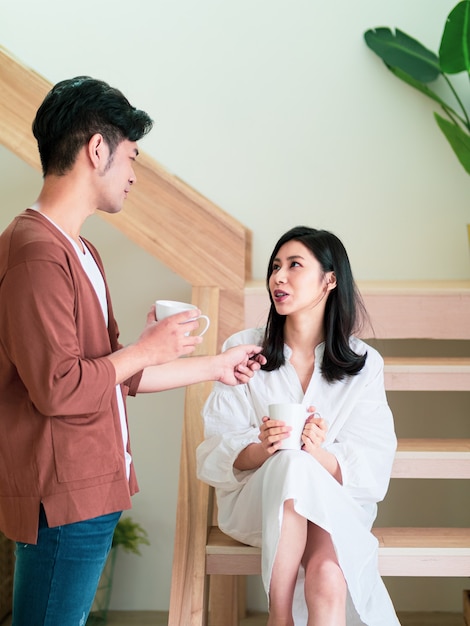 Une jeune femme et un homme asiatiques aiment passer du temps ensemble à la maison avec une tasse de café dans les mains.