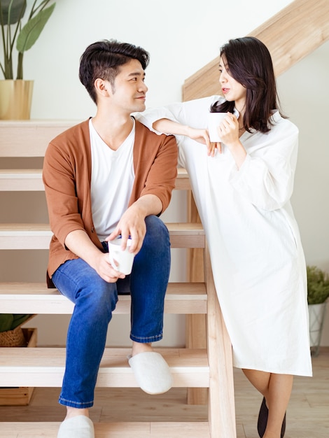 Une jeune femme et un homme asiatiques aiment passer du temps ensemble à la maison avec une tasse de café dans les mains.