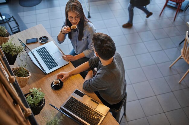 Jeune femme et homme dans un café avec des ordinateurs portables parlant et buvant un expresso