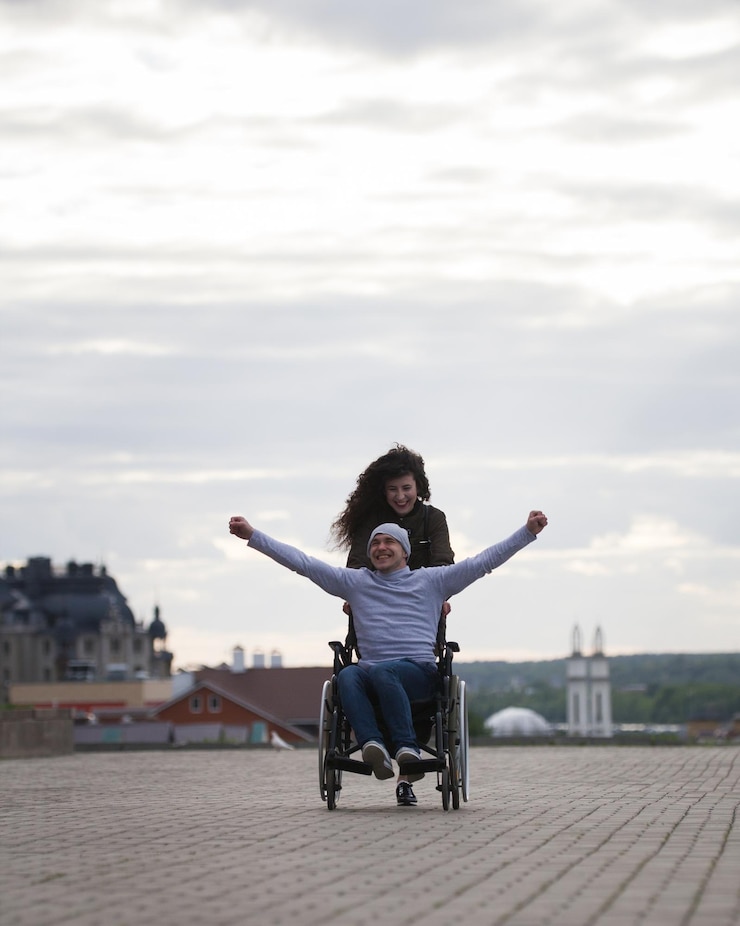 Photo jeune femme avec un homme handicapé heureux en fauteuil roulant s'amusant à l'extérieur