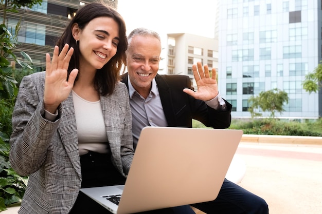 Jeune femme et homme de race blanche saluent l'appel vidéo professionnel assis sur un banc à l'extérieur des immeubles de bureaux Espace de copie Concept technologique