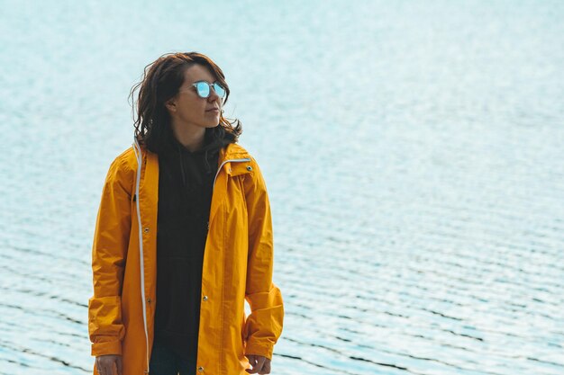 Jeune femme en imperméable jaune devant l'eau