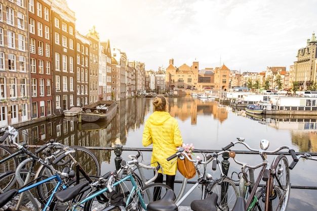 Photo jeune femme en imperméable jaune profitant de la vue matinale sur la magnifique vue sur la ville d'amsterdam