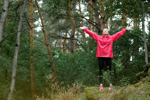 Jeune femme en imperméable rose, faire des exercices de yoga en forêt.