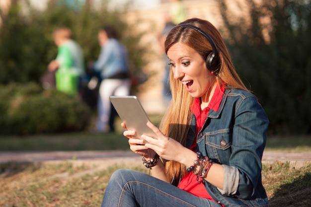 Jeune femme impressionnée et excitée en écoutant de la musique sur la tablette