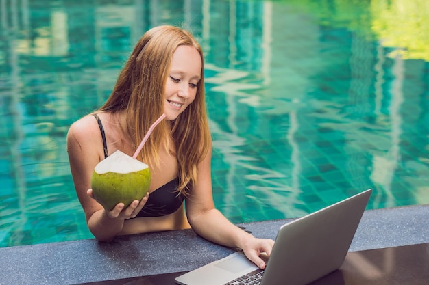 Jeune femme indépendante assise près de la piscine avec son ordinateur portable à l'hôtel en train de naviguer en elle