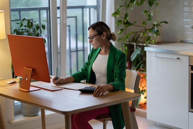 Une jeune femme indépendante concentrée dans des lunettes travaille et rédige une liste pour un nouveau projet au bureau à domicile