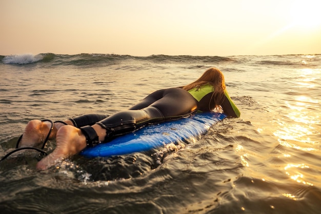 Jeune femme indépendante dans une combinaison de plongée nageant sur une planche de surf dans l'eau à la plage. Fille de surfeur se relaxant dans la romance au coucher du soleil de l'île paradisiaque et la liberté indépendante dans l'océan Indien.