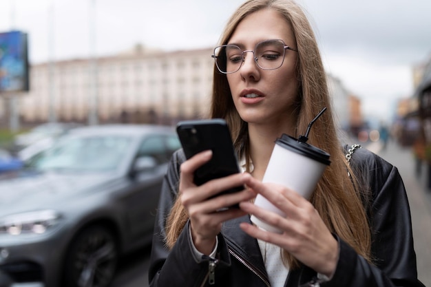 Jeune femme indépendante avec un téléphone dans les mains tout en déjeunant dans la rue