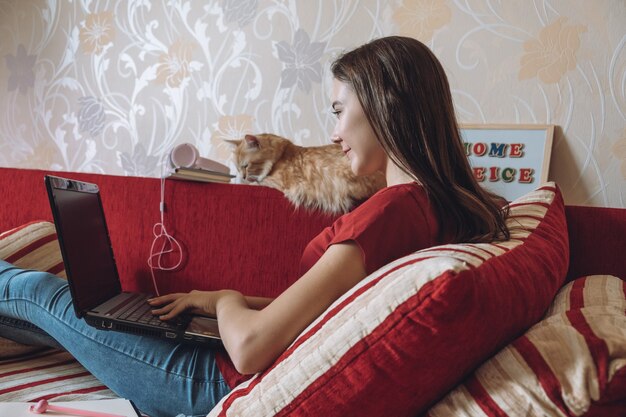 Jeune femme indépendante travaillant dans un bureau à domicile avec un ordinateur portable et un chat travaillant en ligne à distance