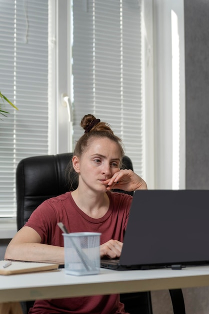 Une jeune femme indépendante travaille à domicile. La fille est assise sur le lieu de travail, travaille sur un ordinateur portable, fatiguée de prendre sa tête. Cadre vertical.