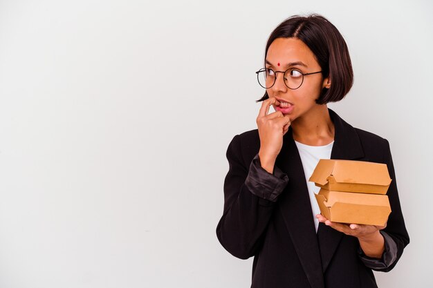 Jeune femme indienne d'affaires mangeant des hamburgers isolés détendue en pensant à quelque chose en regardant un espace de copie.