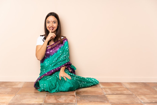 Jeune femme indienne assise sur le sol montrant un signe de silence geste mettant le doigt dans la bouche