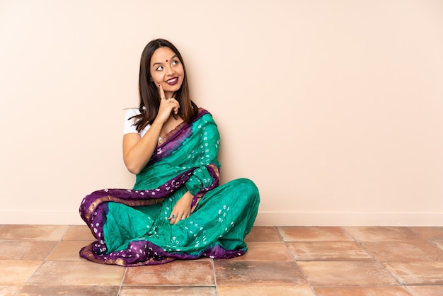 Jeune femme indienne assise sur le sol en pensant à une idée tout en levant les yeux