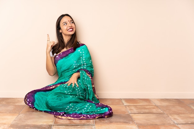 Jeune femme indienne assise sur le sol pointant vers le haut une excellente idée