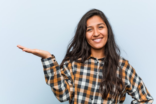 Jeune femme indienne cool montrant sur une paume et tenant une autre main sur la taille.