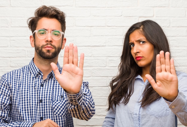 Jeune femme indienne et couple homme caucasien sérieux et déterminé, mettant la main devant, arrêter le geste, nier le concept