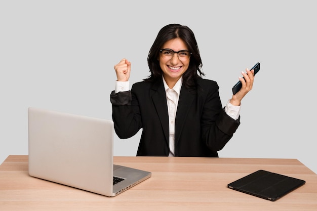 Jeune femme indienne dans une table avec un ordinateur portable et une tablette à l'aide d'un téléphone portable isolé