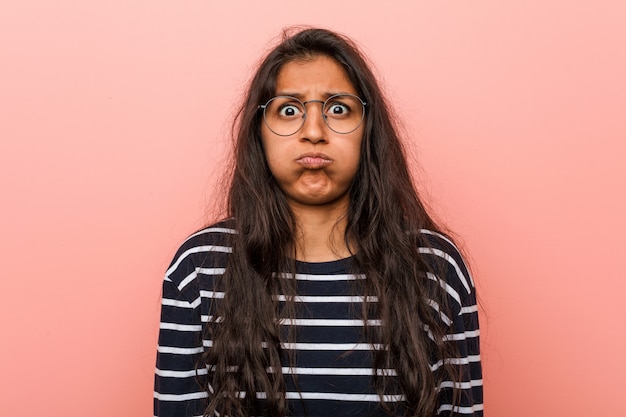 Jeune femme indienne intellectuelle souffle sur les joues, a l'air fatigué. Concept d'expression faciale.