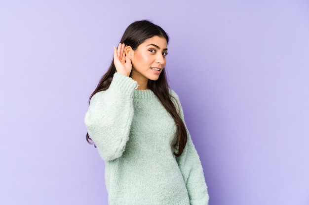 Jeune femme indienne isolée sur l'espace violet essayant d'écouter un potin.