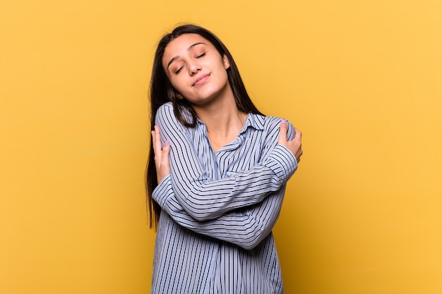 Jeune femme indienne isolée sur des étreintes de mur jaune, souriant insouciant et heureux