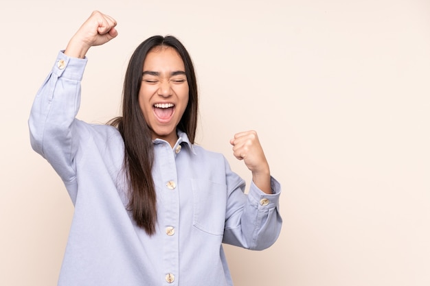 Jeune femme indienne isolée sur fond beige célébrant une victoire