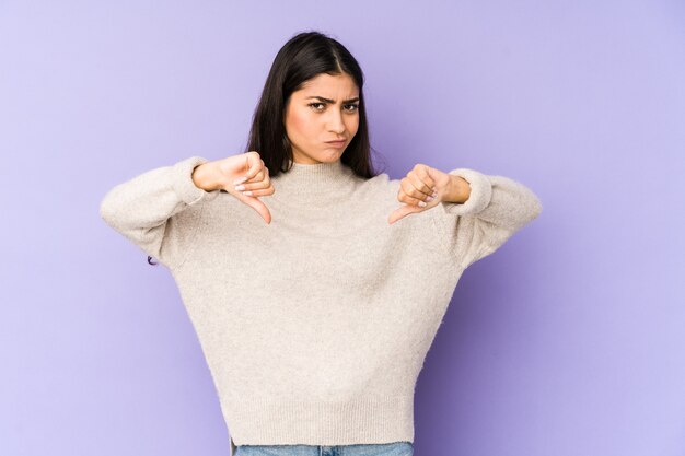 Jeune femme indienne isolée sur fond violet montrant le pouce vers le bas, concept de déception.