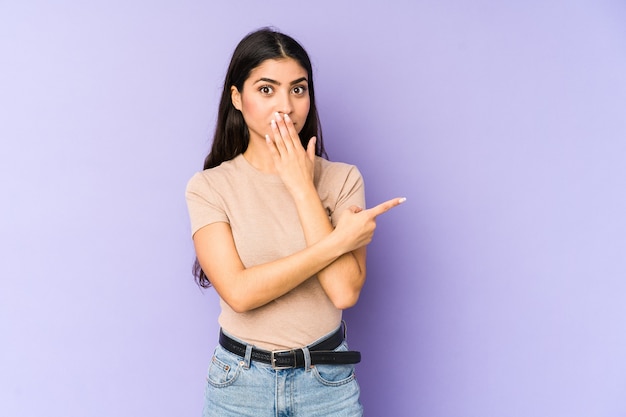 Jeune femme indienne isolée sur fond violet pointant vers le côté