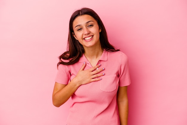 Jeune femme indienne isolée sur un mur rose éclate de rire en gardant la main sur la poitrine.