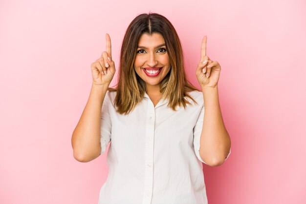 Jeune femme indienne isolée sur un mur rose indique avec les deux doigts avant montrant un espace vide.