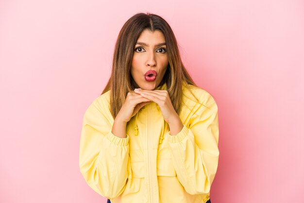 Jeune femme indienne isolée sur un mur rose priant pour la chance, étonné et ouvrant la bouche à l'avant.