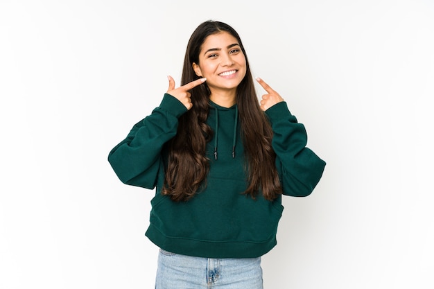 Jeune femme indienne isolée sur des sourires violets, pointant les doigts sur la bouche.