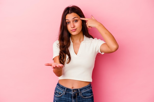 Jeune femme indienne isolée sur la tenue rose et montrant un produit à portée de main.