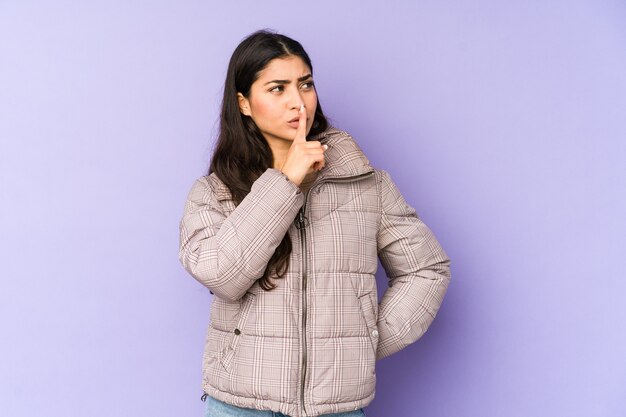 Jeune femme indienne isolée sur violet gardant un secret ou demandant le silence.