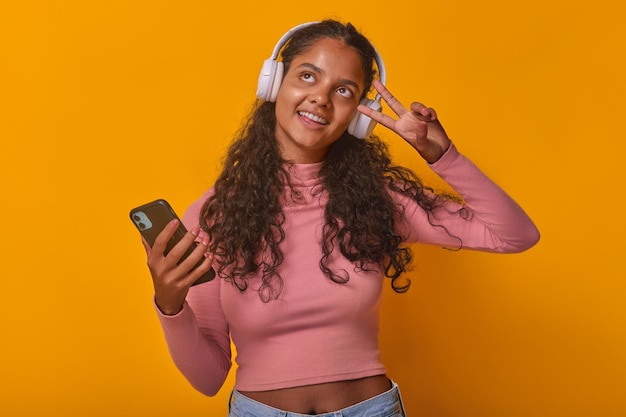 Une jeune femme indienne joyeuse dans des écouteurs écoute de la musique en utilisant un téléphone portable