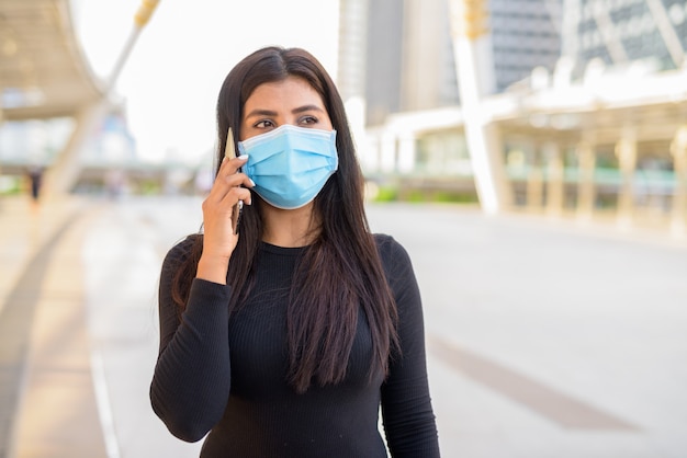 Jeune femme indienne avec masque parlant au téléphone au pont skywalk