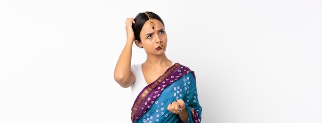 Jeune femme indienne sur mur blanc ayant des doutes en se grattant la tête