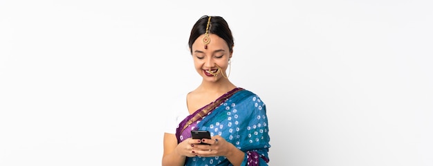 Jeune femme indienne sur mur blanc en envoyant un message avec le mobile