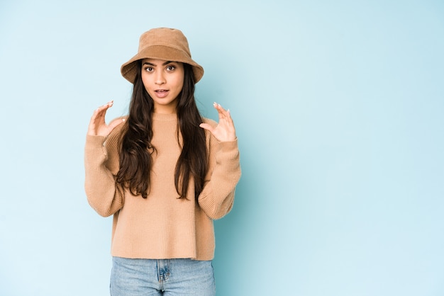 Jeune femme indienne portant un chapeau isolé sur bleu tenant quelque chose avec des paumes