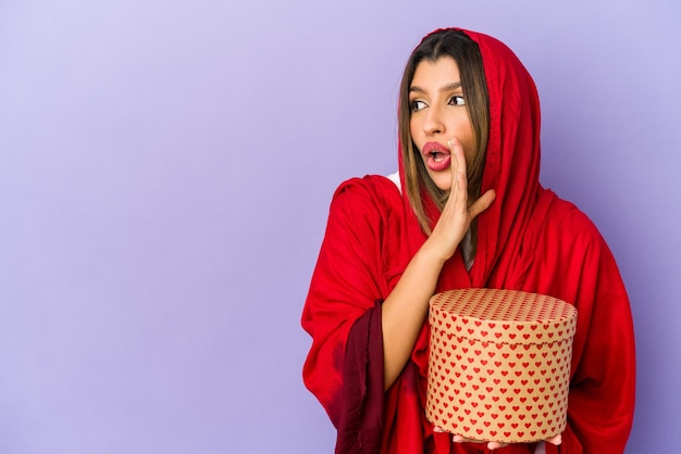 Jeune femme indienne portant un hijab tenant un cadeau de la Saint-Valentin isolé dit un secret de freinage à chaud et à côté