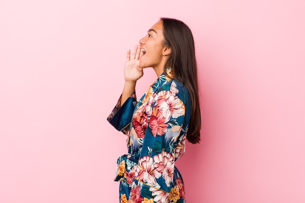 Jeune femme indienne portant un pyjama kimono criant et tenant la paume près de la bouche ouverte.