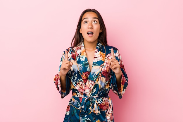 Jeune femme indienne portant un pyjama kimono pointant à l'envers avec la bouche ouverte.