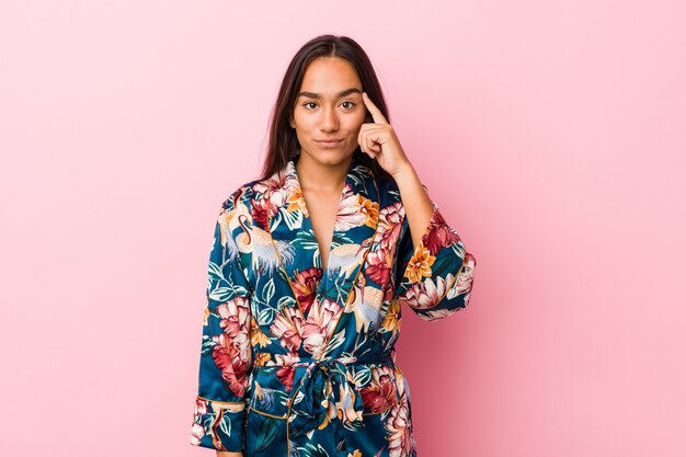 Jeune femme indienne portant un pyjama kimono pointant le temple avec le doigt, pensant, concentré sur une tâche.