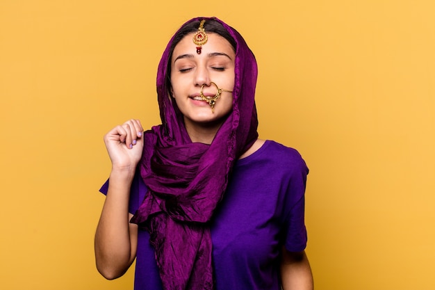 Jeune femme indienne portant un sari traditionnel isolé sur fond jaune dansant et s'amusant.