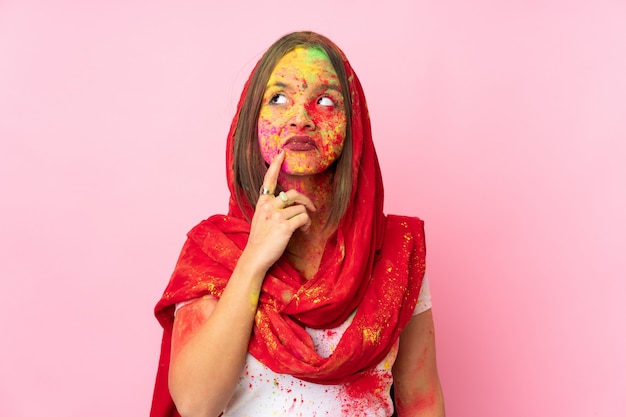 Jeune femme indienne avec des poudres de holi colorées sur son visage isolé sur mur rose ayant des doutes et de la pensée