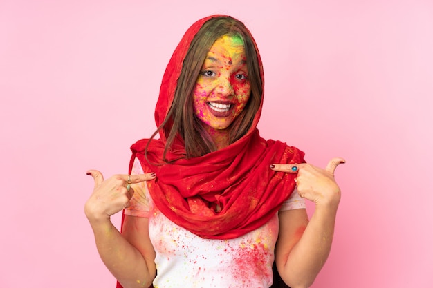 Jeune femme indienne avec des poudres de holi colorées sur son visage isolé sur un mur rose donnant un coup de pouce vers le haut