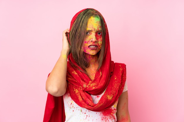 Jeune femme indienne avec des poudres de holi colorées sur son visage sur le mur rose ayant des doutes