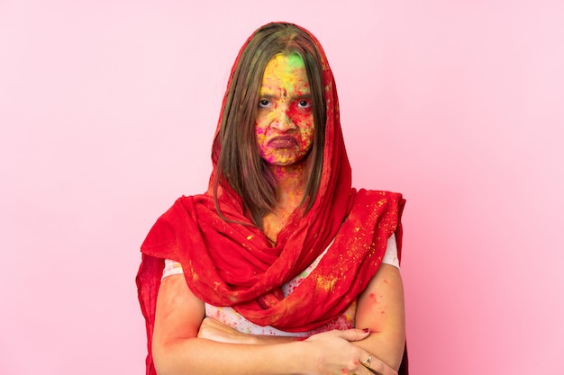 Jeune femme indienne avec des poudres de holi colorées sur son visage sur un mur rose avec une expression malheureuse