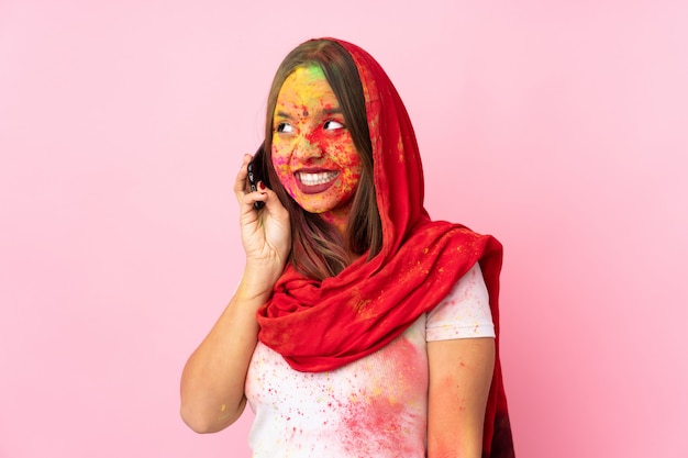 Jeune femme indienne avec des poudres de holi colorées sur son visage sur le mur rose en gardant une conversation avec le téléphone mobile